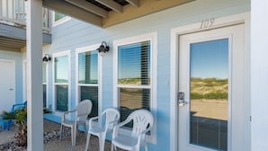 Een huis aan de kust met het cijfer 109 op de deur, een overdekte veranda met witte stoelen en uitzicht op het strand door de ramen.