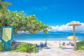 Relax on the beach with comfortable seating and umbrellas, surrounded by calm waters and safety signs.