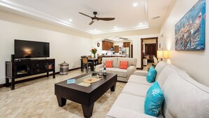 A living room with a TV, dark coffee table, light-colored sofa, and a ceiling fan. - Horizontes del Mar 105♆Beachfront♆ Easy Beach access, security & cameras (Playa Langosta)