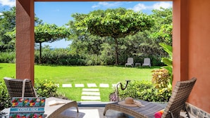 A patio area with wicker furniture, a bag labeled "Costa Rica," and a view of a lush garden and trees. - Horizontes del Mar 105♆Beachfront♆ Easy Beach access, security & cameras (Playa Langosta)
