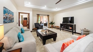 A living room with a sofa, armchairs, a coffee table, a TV, and a ceiling fan. - Horizontes del Mar 105♆Beachfront♆ Easy Beach access, security & cameras (Playa Langosta)
