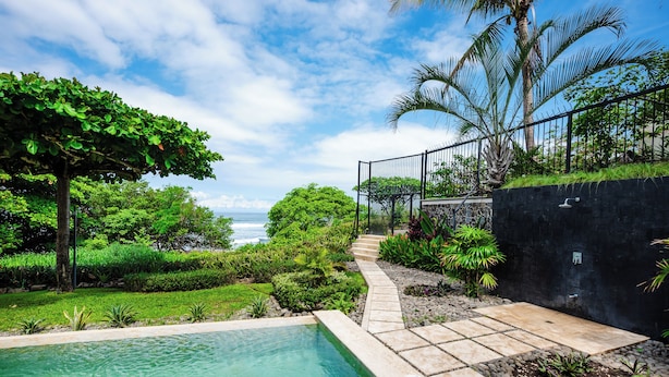 A pool area with a view of the ocean, surrounded by lush greenery and a stone pathway. - Horizontes del Mar 105♆Beachfront♆ Easy Beach access, security & cameras (Playa Langosta)