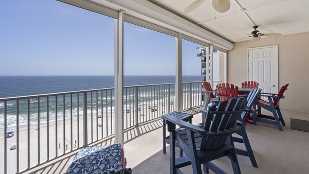 A balcony with a view of the ocean, equipped with ceiling fans and red and blue Adirondack chairs.