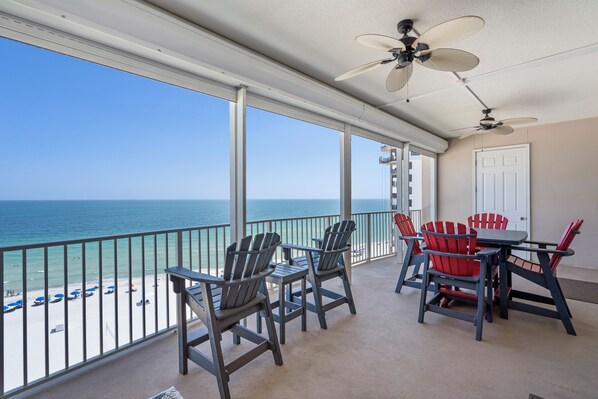 A balcony with a view of the ocean, featuring ceiling fans, chairs, and a table.
