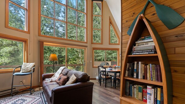Een ruime woonkamer met een leren bank, een houten boekenkast en grote ramen met uitzicht op het landschap.