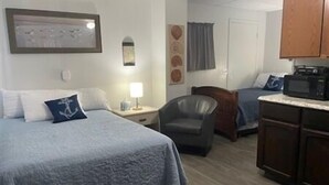 Ett hotellrum med en säng, en stol, ett skrivbord, en mikrovågsugn och ett skåp.