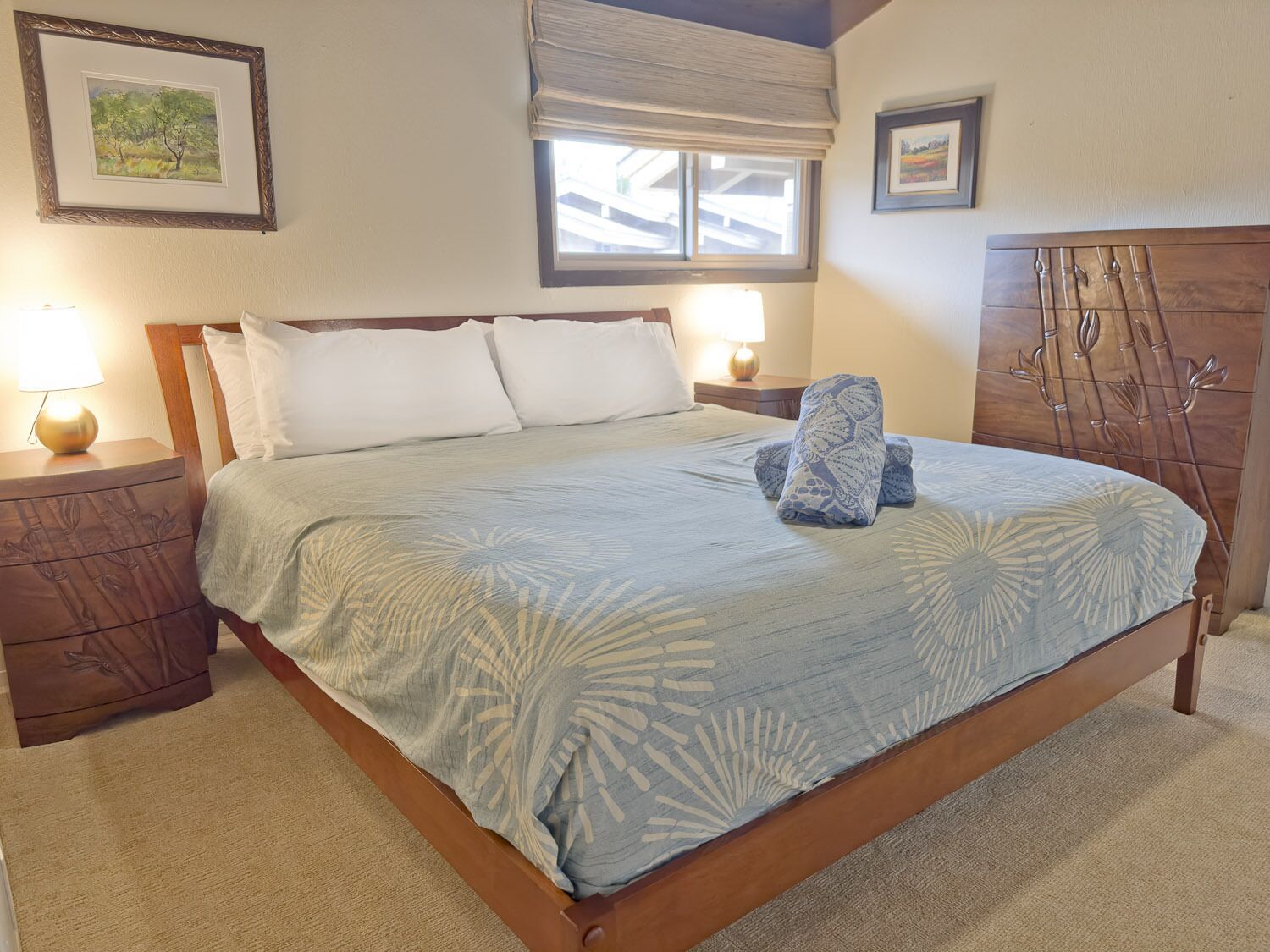 A neatly made bed with a floral-patterned bedspread, two bedside lamps, and a window with a view of the outside.