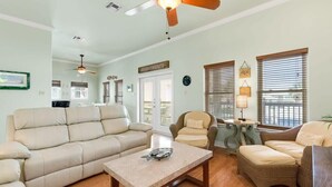 A living room with a beige sofa, a coffee table, and wicker chairs. - Island Breeze Home, Dual Pools & Private Decks (Port Aransas)