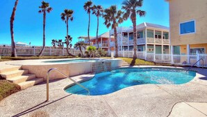 A swimming pool with steps leading into it, surrounded by palm trees and a white fence. - Island Breeze Home, Dual Pools & Private Decks (Port Aransas)
