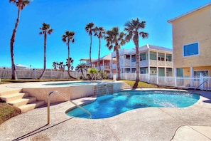 A swimming pool with steps leading into it, surrounded by palm trees and a white fence.
