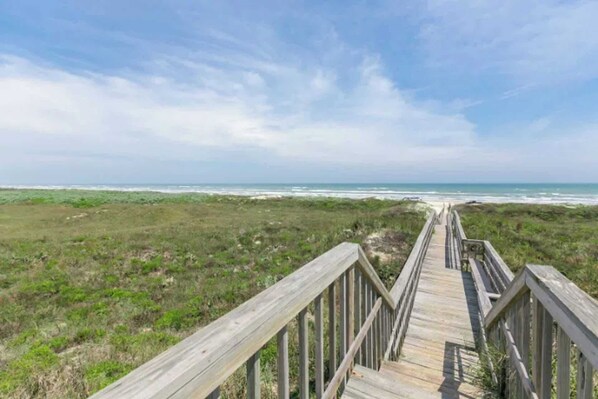 A wooden boardwalk leading to a beach with a clear sky.