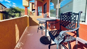 A balcony with a round table and two chairs, a red wall, and a window with blinds. - Sunset Sands by Mesquite Vacation Rentals: Pet Friendly near Wolf Creek with $510 in free daily activities (Mesquite)