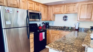 A kitchen with wooden cabinets, a stainless steel refrigerator, a microwave, a stove, and a granite countertop. - Sunset Sands by Mesquite Vacation Rentals: Pet Friendly near Wolf Creek with $510 in free daily activities (Mesquite)