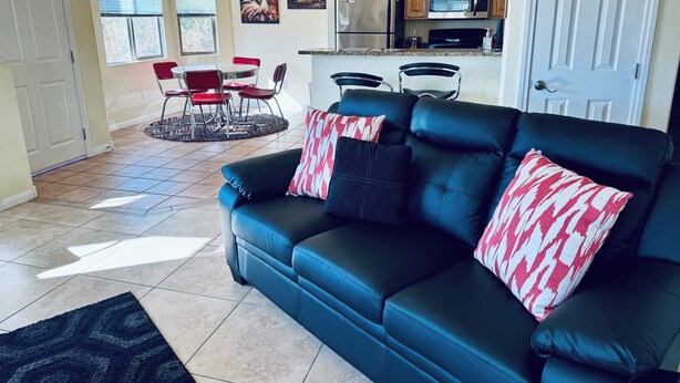 A living room with a black leather sofa, red and white patterned pillows, a black rug, and a dining area with red chairs and a glass table. - Sunset Sands by Mesquite Vacation Rentals: Pet Friendly near Wolf Creek with $510 in free daily activities (Mesquite)
