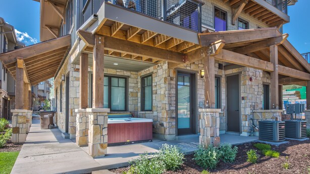 A stone building with a covered patio, outdoor seating, and air conditioning units. - Modern Mountainside Townhome, Natural Light, Outdoor Recreation + Hot Tub! (Park City)