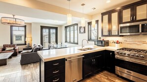 A modern kitchen with a central island, stainless steel appliances, and a dining area with a sofa and table. - Modern Mountainside Townhome, Natural Light, Outdoor Recreation + Hot Tub! (Park City)