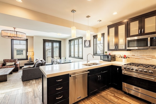 A modern kitchen with a central island, stainless steel appliances, and a dining area with a sofa and table.
