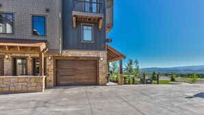 A two-story house with a stone facade, a wooden garage door, and a balcony. - Modern Mountainside Townhome, Natural Light, Outdoor Recreation + Hot Tub! (Park City)