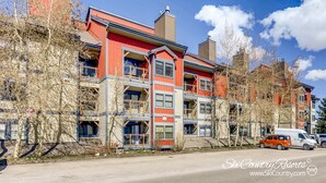 A multi-story building with balconies, a parking area, and a clear sky. - Perfect Downtown Retreat with ALL NEW APPLIANCES AS OF FALL 2025! (Breckenridge)