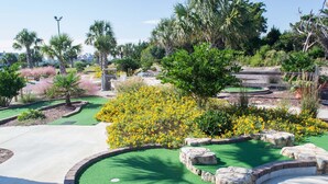 A well-maintained golf course with a putting green, surrounded by lush greenery and flowering plants.