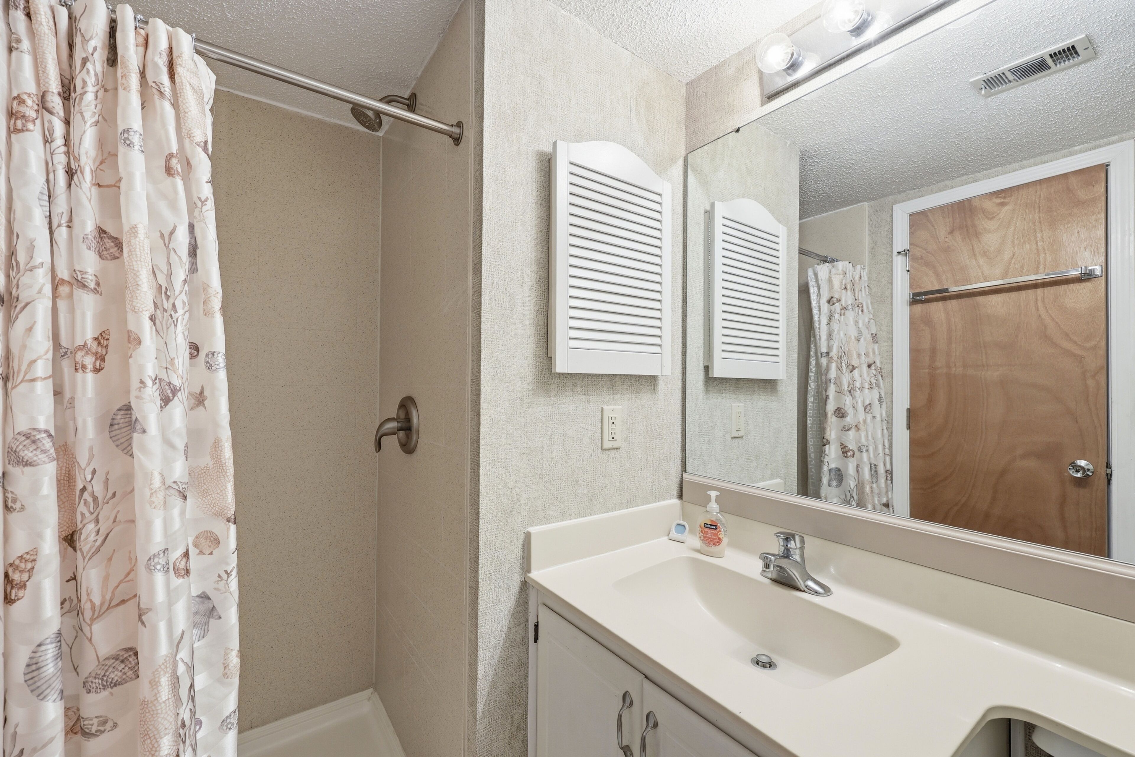Une salle de bain avec un rideau de douche, un miroir, un lavabo et une porte en bois.