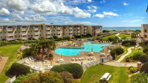 A hotel with a large swimming pool, multiple balconies, and a view of the sea.