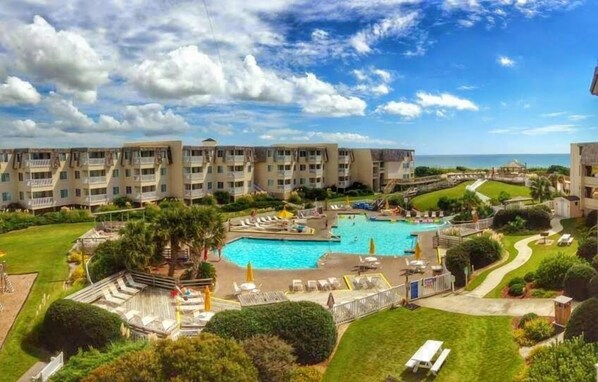 A hotel with multiple balconies, a central swimming pool, and a landscaped garden.