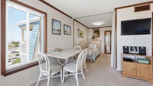 A room with a dining table, chairs, a bed, a TV, and a cabinet.