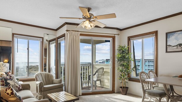 A spacious living room with a ceiling fan, a dining table, and a balcony with a view of the city.