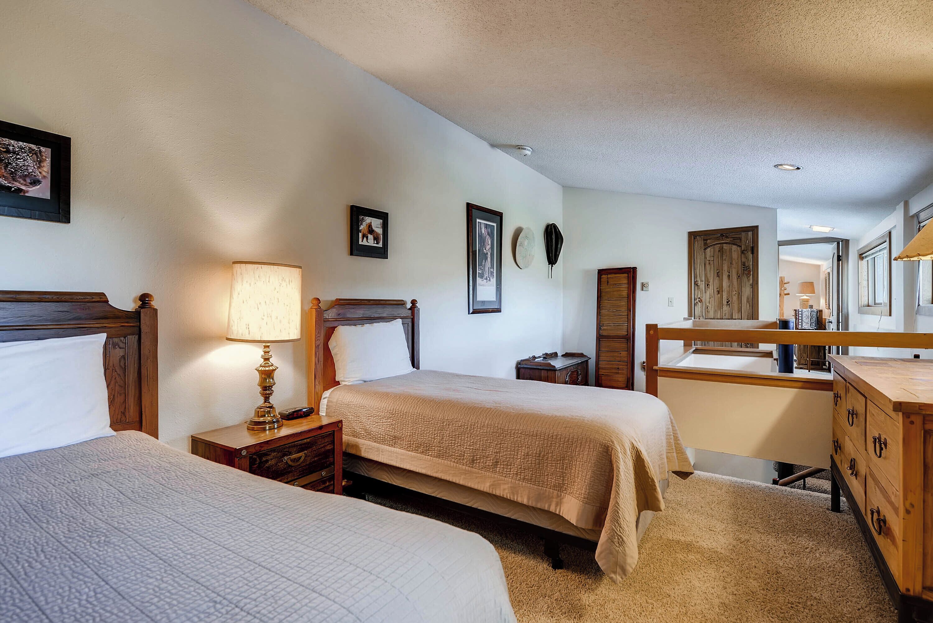 A hotel room with two beds, a wooden dresser, a desk, and a lamp.