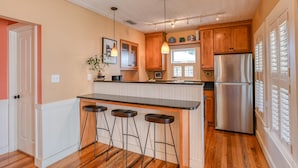 A kitchen with wooden cabinets, a stainless steel refrigerator, a bar counter with stools, and pendant lighting. - Historic Downtown Cottage with Private/Heated Pool! Walk to everything! (st. augustine)