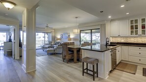 A modern kitchen with a large island, white cabinetry, and a dining area with wicker furniture.