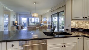 A modern kitchen with a large island, white cabinetry, and a view to the outdoors.