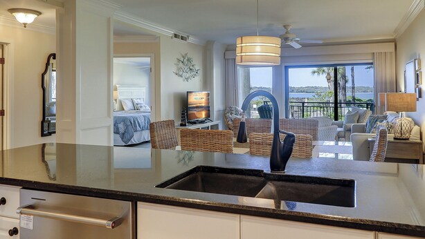 A modern kitchen with a large island, a dining area with wicker furniture, and a view of the ocean through large windows.