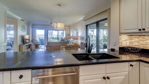 Une cuisine moderne dotée d’un grand îlot central, de meubles blancs et offrant une vue sur l’extérieur.