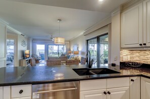 Una cocina moderna con una isla grande, armarios blancos y vistas al exterior.
