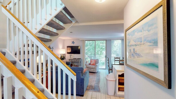 A staircase with wooden handrails and a view of a living room with a sofa, a television, and a painting of a beach scene. - Villa 212 3 bedrooms, 2 bathroom (Jekyll Island)