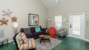 A living room with a dark sofa, a colorful striped chair, a small wooden table, and a teal floor. - Poolside Coastal Retreat | Short Walk to the Beach (Corpus Christi)