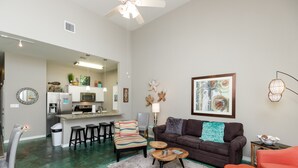 A spacious living area with a dark brown sofa, colorful striped chair, and a wooden coffee table. A kitchen is visible in the background with modern appliances. - Poolside Coastal Retreat | Short Walk to the Beach (Corpus Christi)