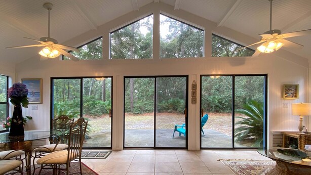 Una habitación amplia con grandes puertas corredizas de vidrio que dan a un área exterior cubierta, una mesa de comedor con sillas y dos ventiladores de techo.