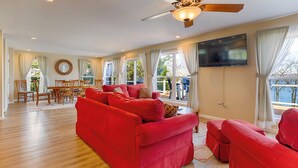 A spacious living room with a red sofa set, a dining area with wooden furniture, large windows with curtains, and a ceiling fan. - Seneca Shores: Attention Wine Trail and Lakefront Enthusiasts! (Himrod)