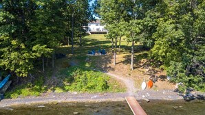 A lakeside property with a dock, a grassy area with outdoor seating, and a house in the background. - Seneca Shores: Attention Wine Trail and Lakefront Enthusiasts! (Himrod)