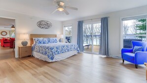 A bedroom with a large bed, a ceiling fan, a view of the outdoors, and a red sofa in the adjacent room. - Seneca Shores: Attention Wine Trail and Lakefront Enthusiasts! (Himrod)
