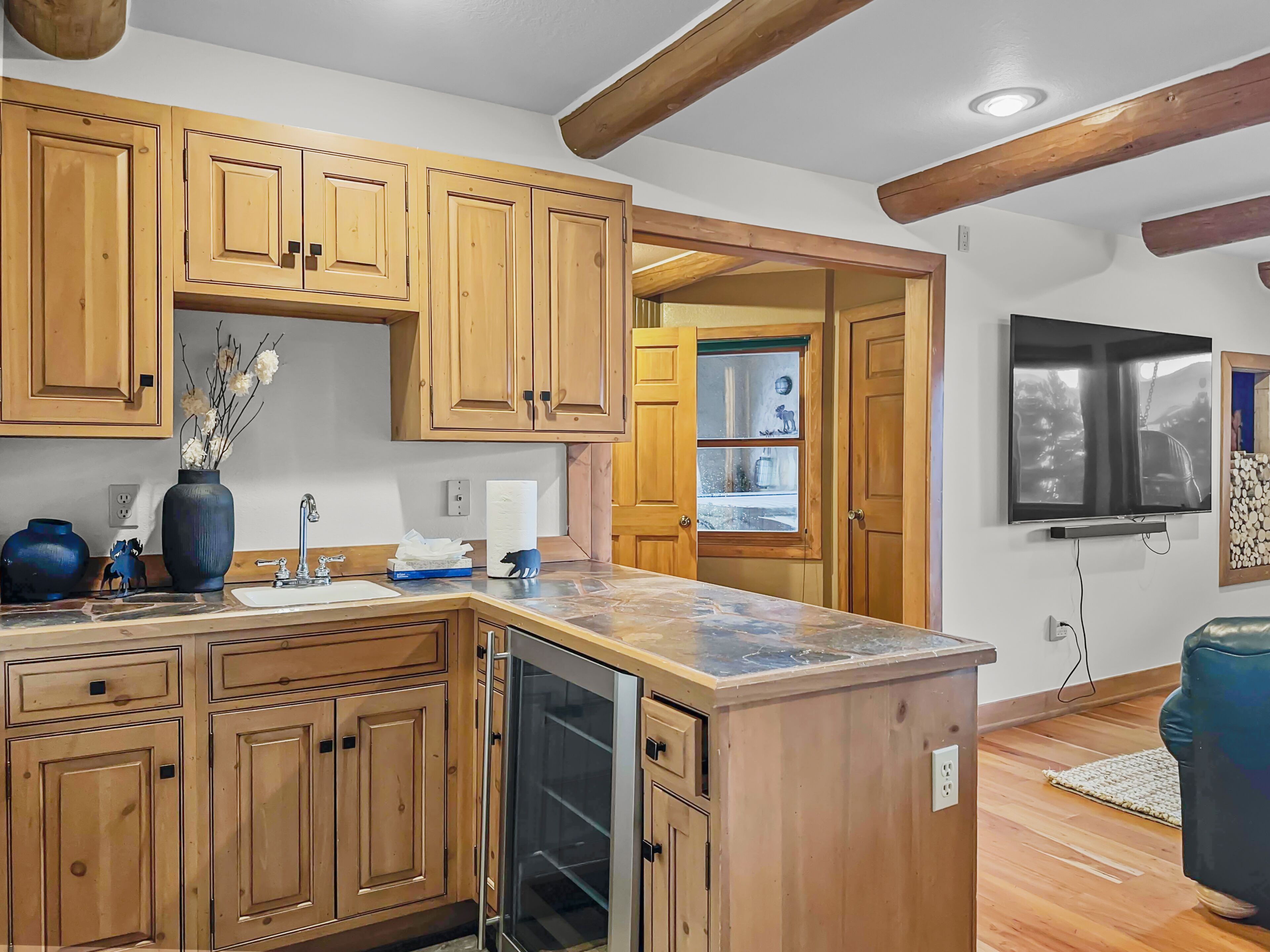 A kitchen with wooden cabinets, a marble countertop, a dishwasher, and a TV mounted on the wall.