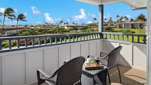 Ein Balkon mit Korbstühlen und einem Tisch, mit Blick auf eine gepflegte Rasenfläche und Gebäude.