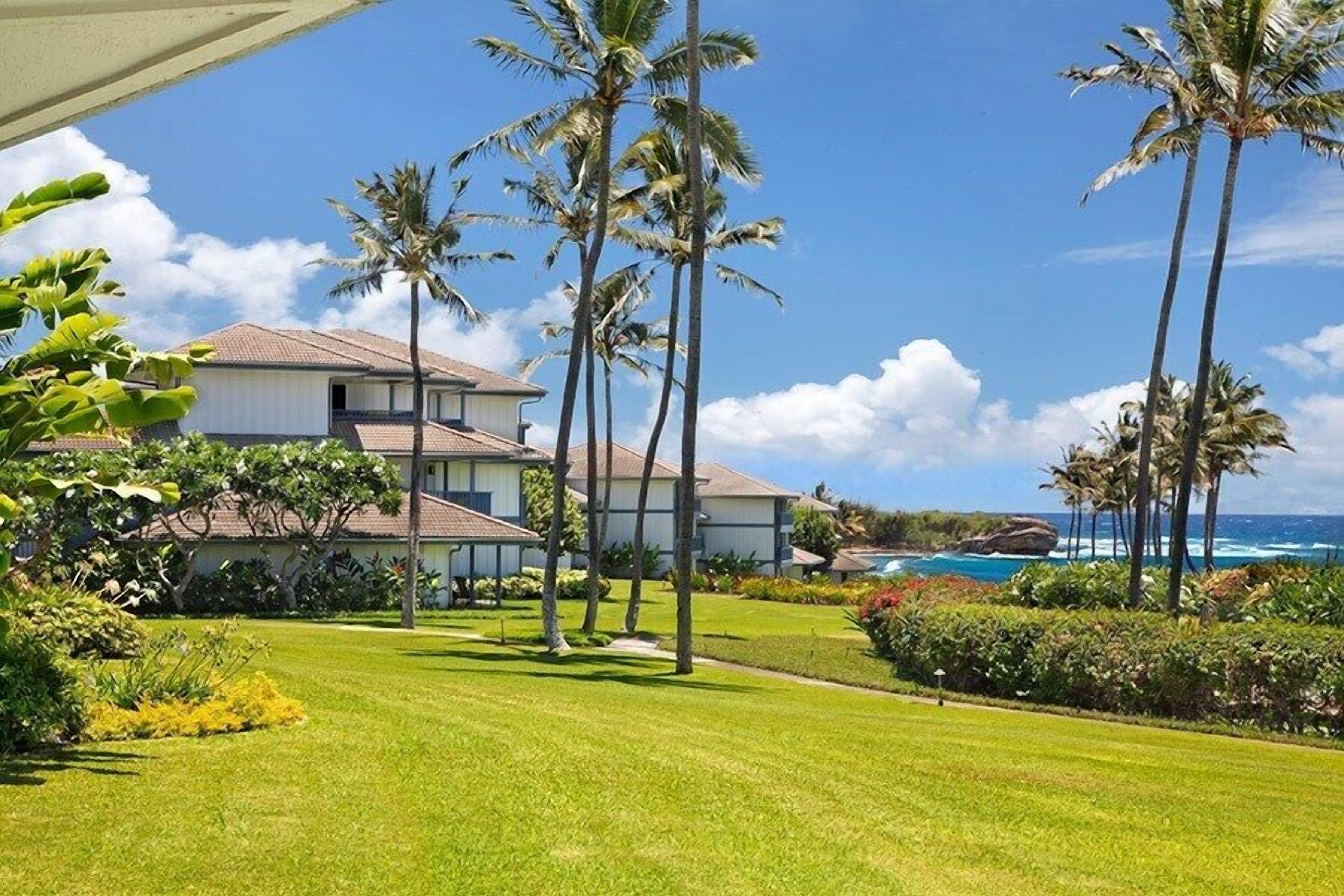 A beachfront property with a two-story building, palm trees, and a clear view of the ocean.