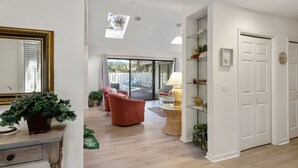 Amplia sala de estar con un sillón rojo, una mesa de centro de vidrio y una lámpara. Hay una puerta corrediza de vidrio que da a un patio exterior.