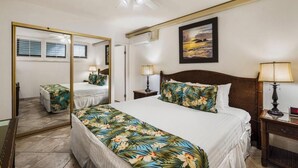 A bedroom with a large bed, a mirror, a ceiling fan, and a framed picture on the wall.