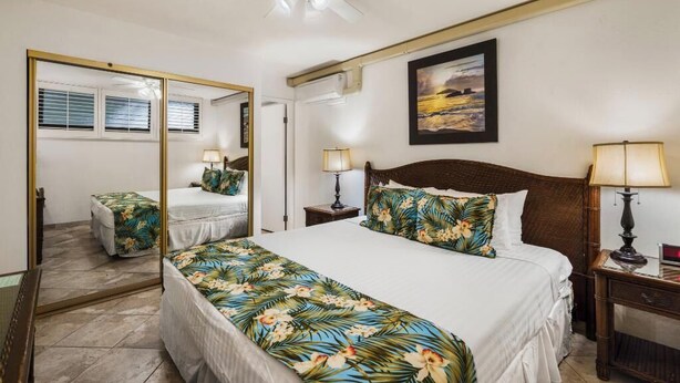 A bedroom with a large bed, a mirror, a ceiling fan, and a framed picture on the wall. - Oceanfront Ground-Floor Retreat: Kihei Surfside #111 – Stunning Views! (Kihei, Maui)