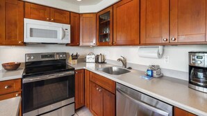 A kitchen with wooden cabinets, a stainless steel stove, a microwave, a sink, and a coffee maker. - Oceanfront Ground-Floor Retreat: Kihei Surfside #111 – Stunning Views! (Kihei, Maui)